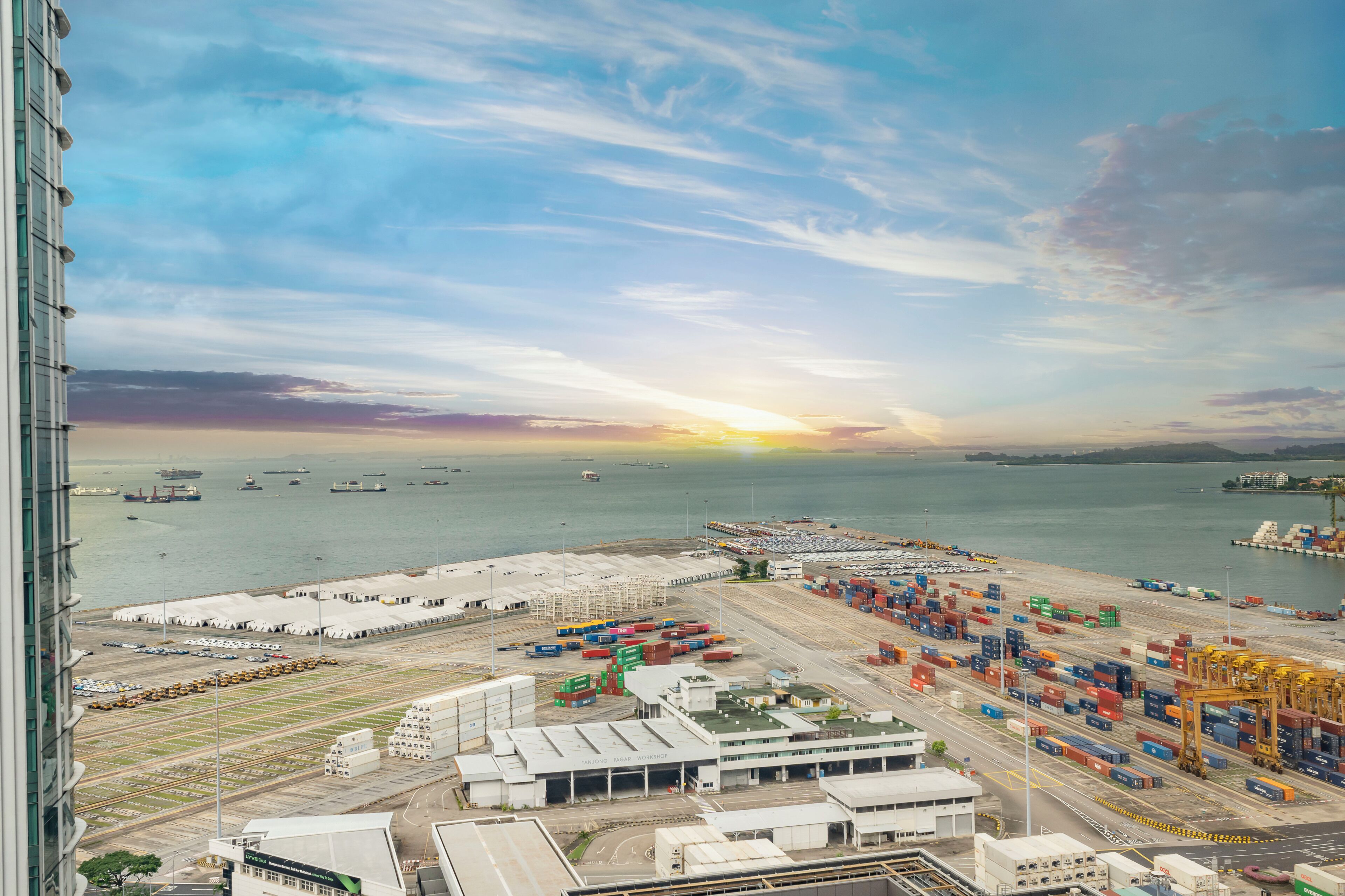 A port area with shipping containers, cranes, and a sunset over the water.