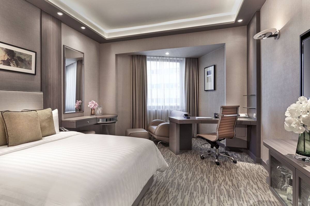 A hotel room with a large bed, a desk, a chair, a mirror, and a television.