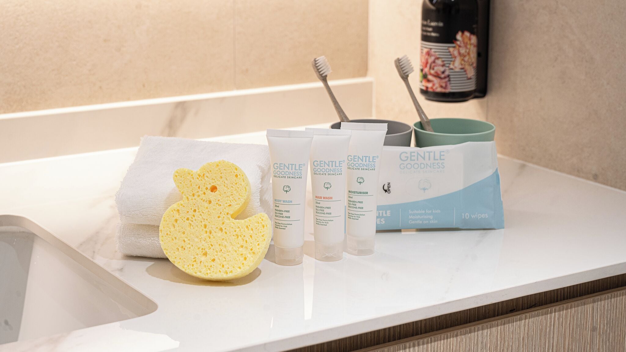Una encimera de baño con una toalla, una esponja y productos de cuidado de la piel Gentle Goodness.