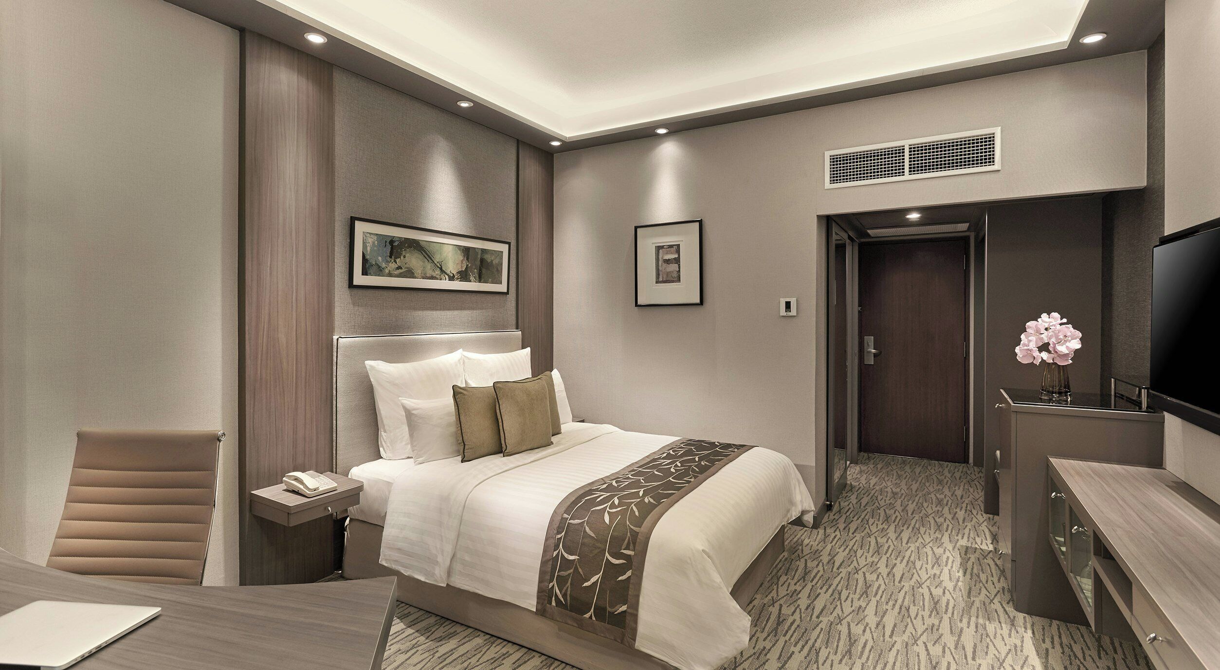 A modern hotel room with a bed, bedside table, chair, desk, and a television.