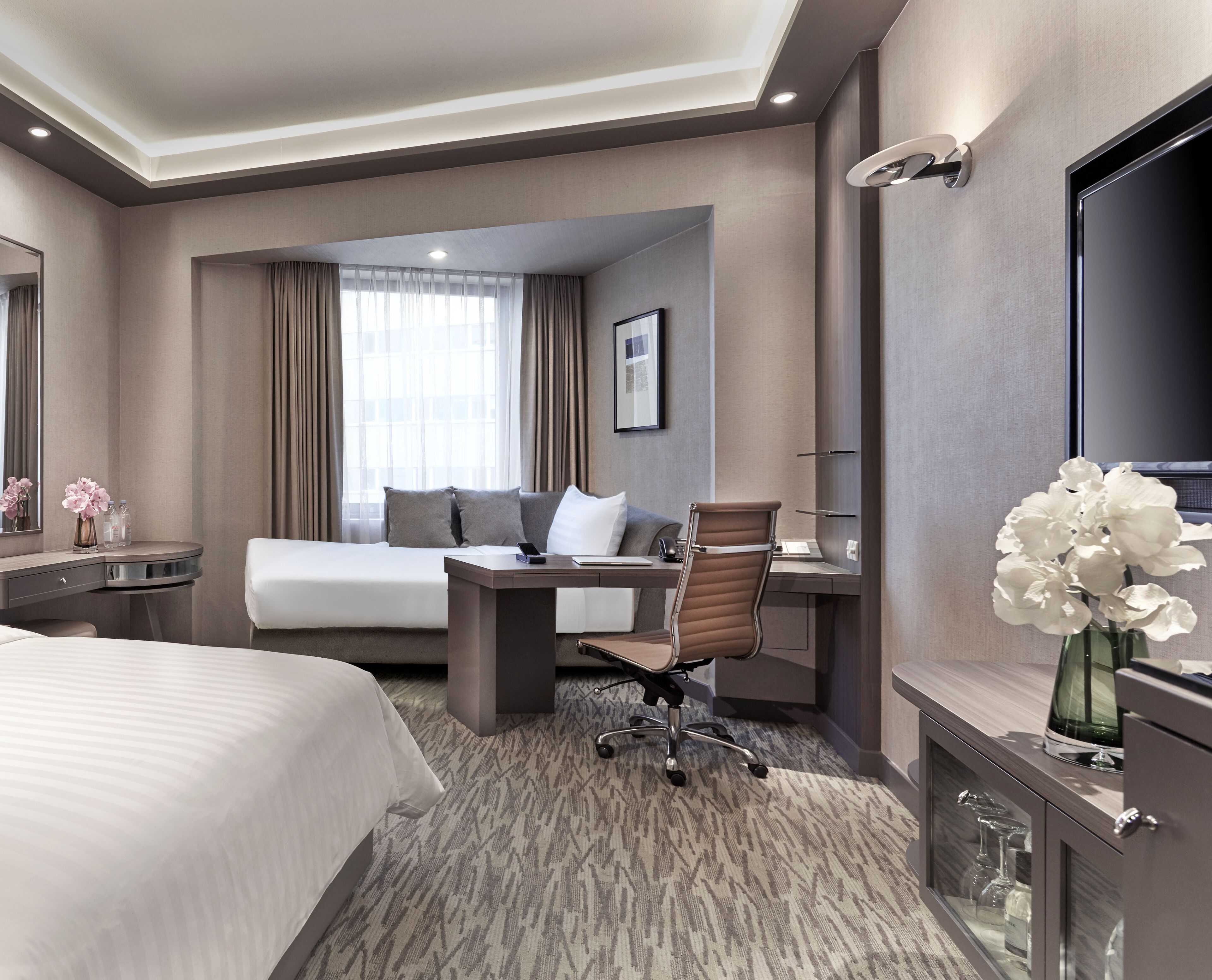 Habitación de hotel con cama, escritorio, silla, televisor y zona de baño.