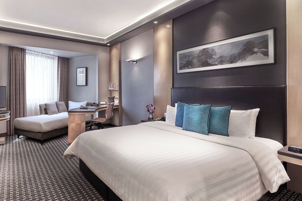 A hotel room with a large bed, a desk, a chair, and a view of the city.