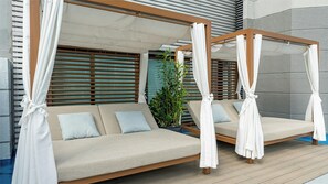 Sofá exterior para dos personas con dosel, colocado frente a un edificio con listones de madera y una planta en maceta cerca.