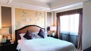 A hotel room with a large bed, two bedside tables, a wall-mounted lamp, and a window with curtains.