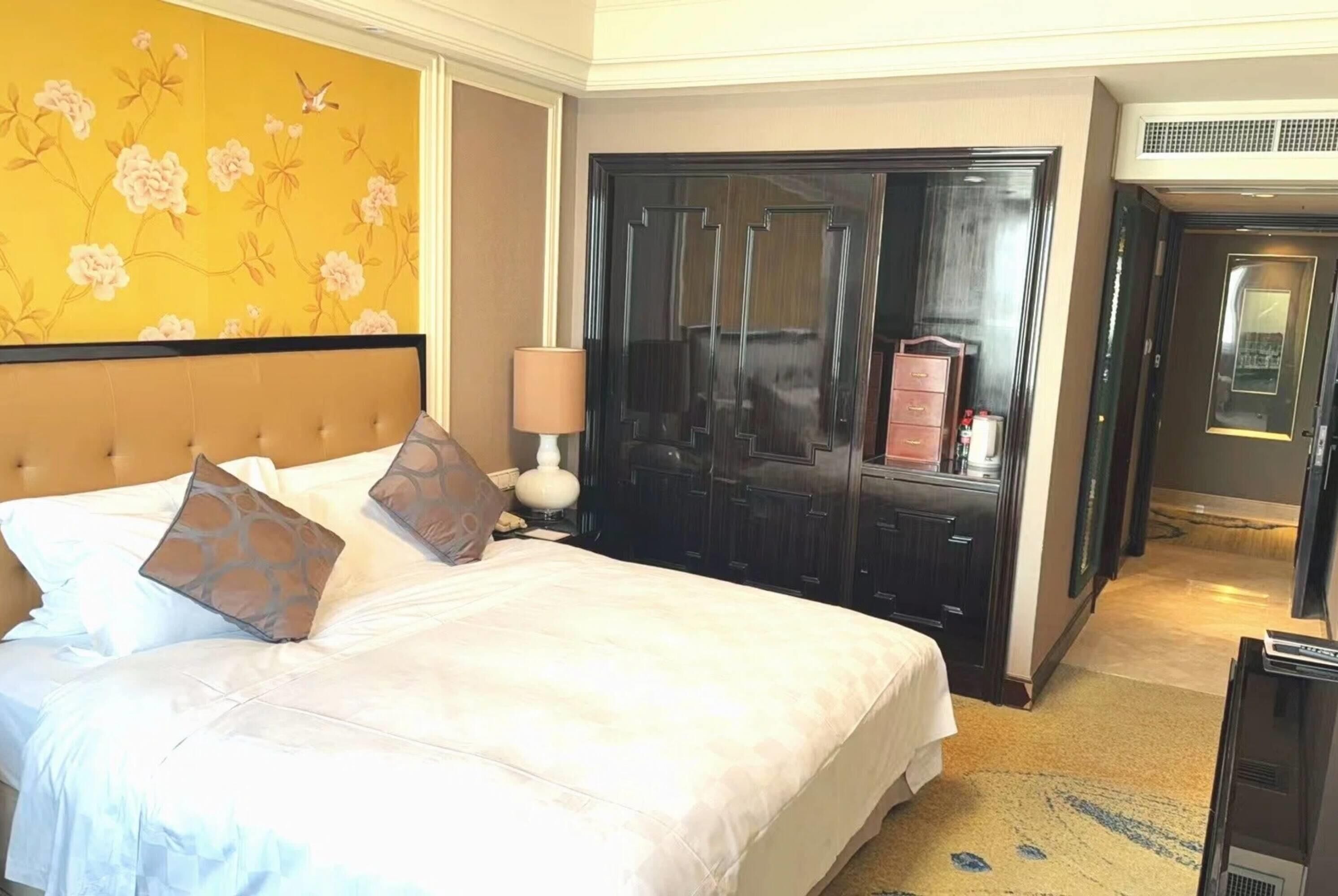 A hotel room with a bed, a wardrobe, a lamp, and a television.