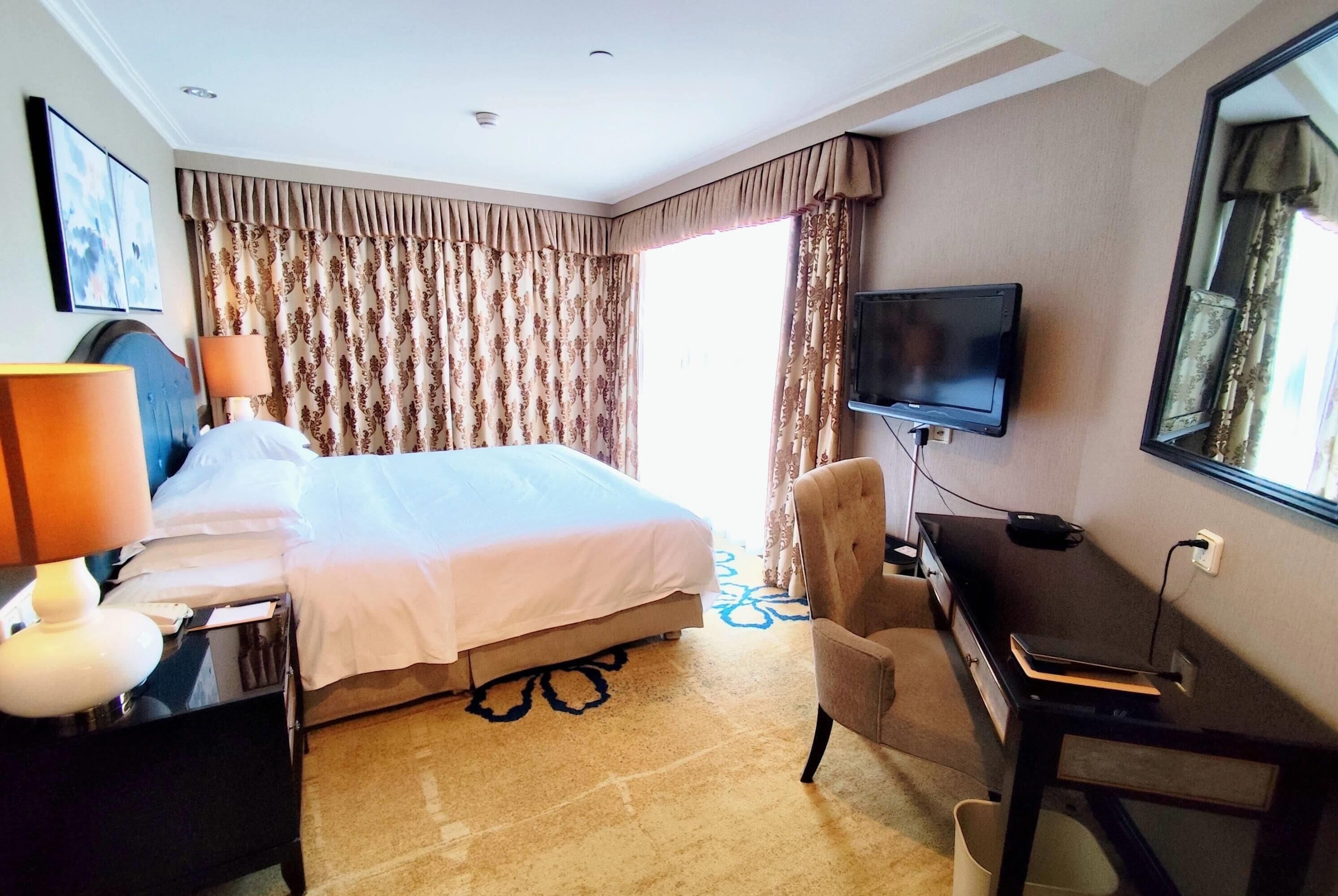 Habitació d'hotel amb llit, escriptori, cadira, televisió i cortines.