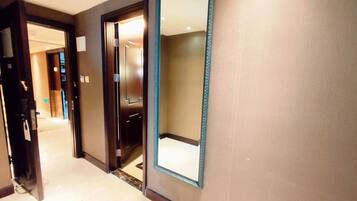 A hotel hallway with a large mirror, a door, and a light switch on the wall.