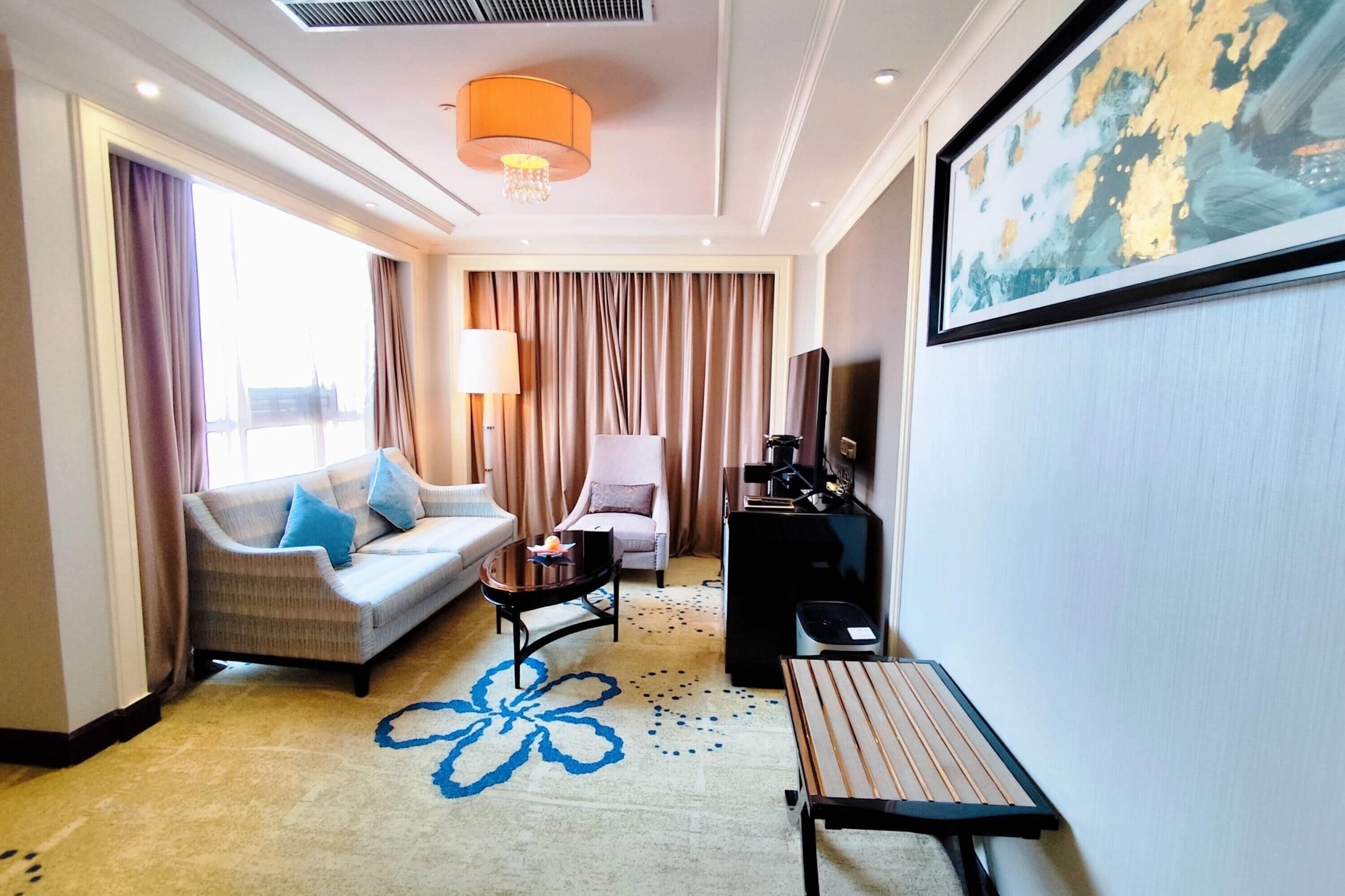 A hotel room with a sofa, armchair, small table, TV, and a painting on the wall.