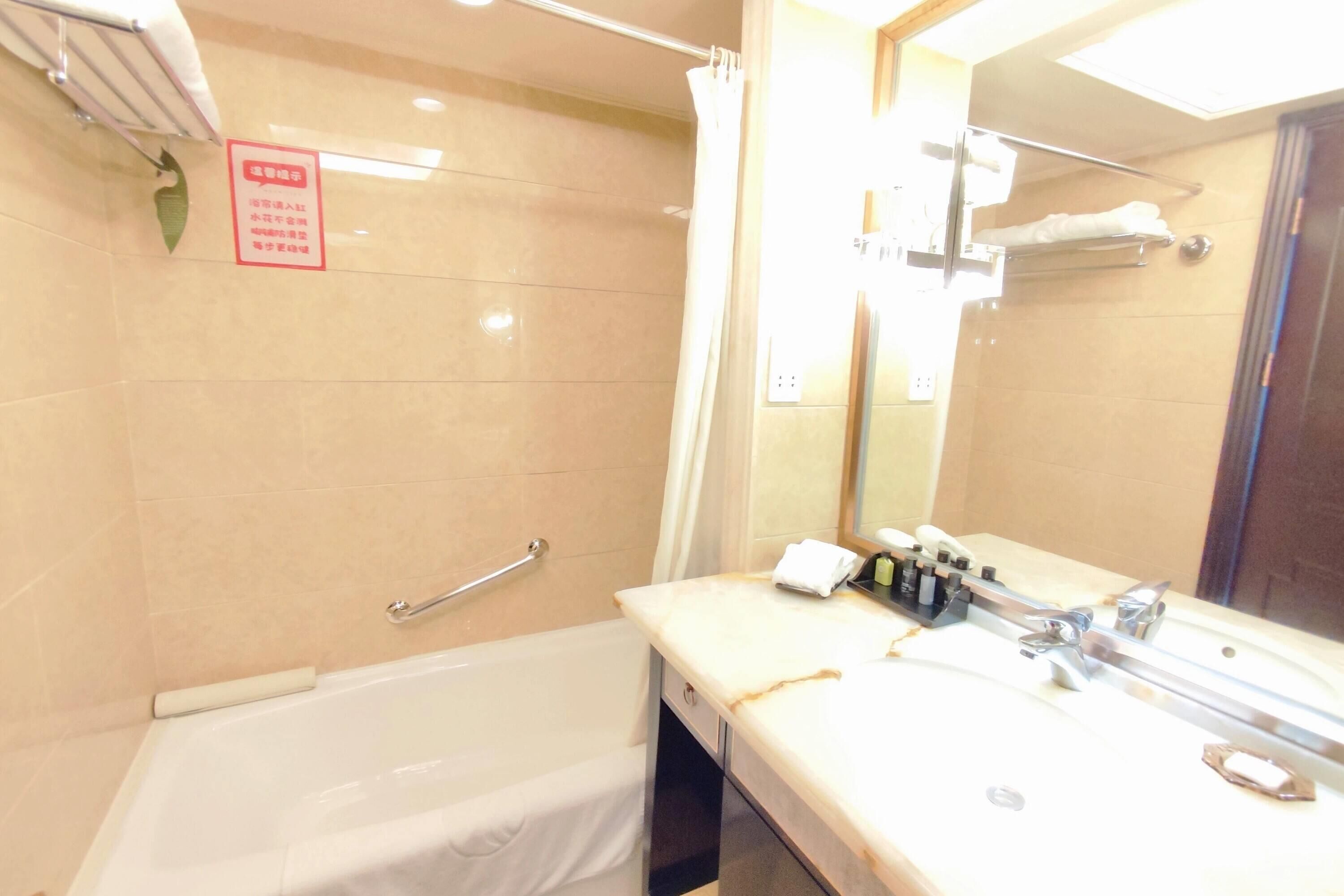 Un baño con bañera, lavamanos con artículos de aseo, toallero y espejo.