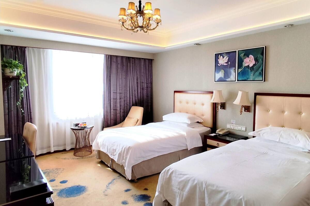 Habitación de hotel con dos camas, un escritorio, una silla, una mesita con fruta y un candelabro.