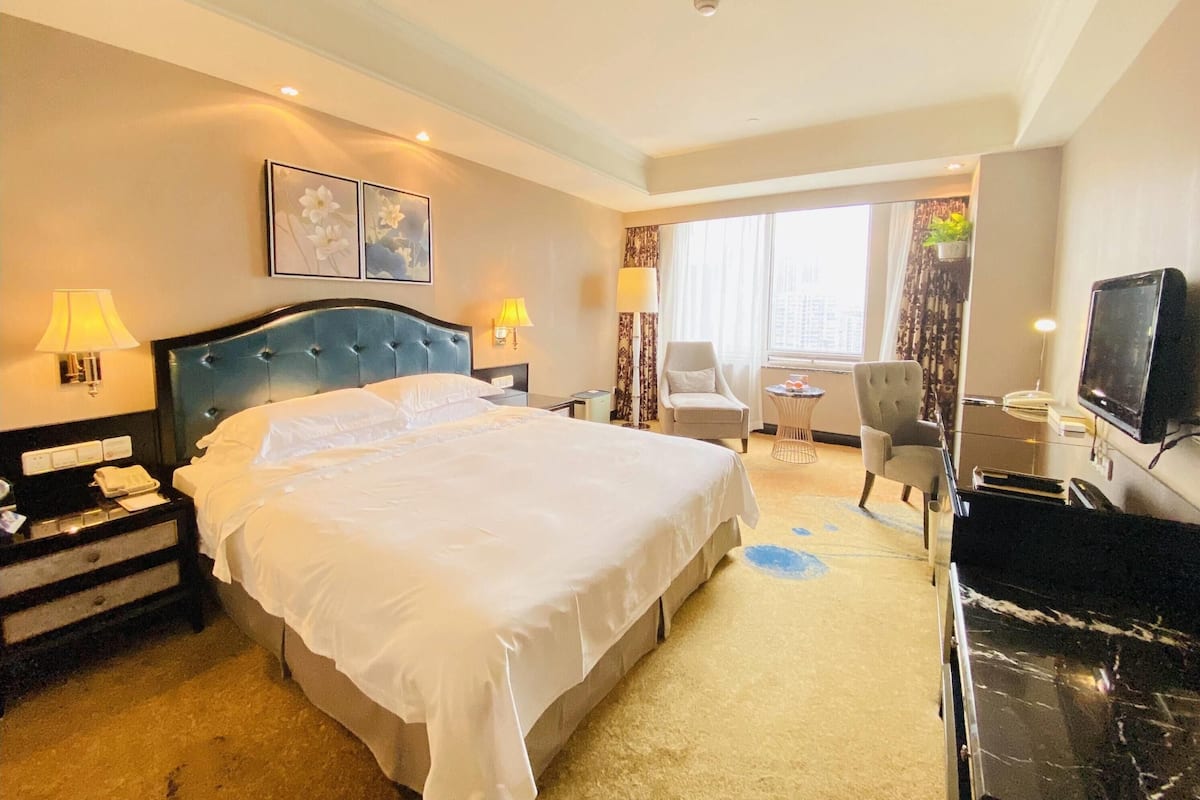 Habitación de hotel con una cama grande, lámparas de noche, un escritorio con silla, un televisor y una ventana con cortinas.