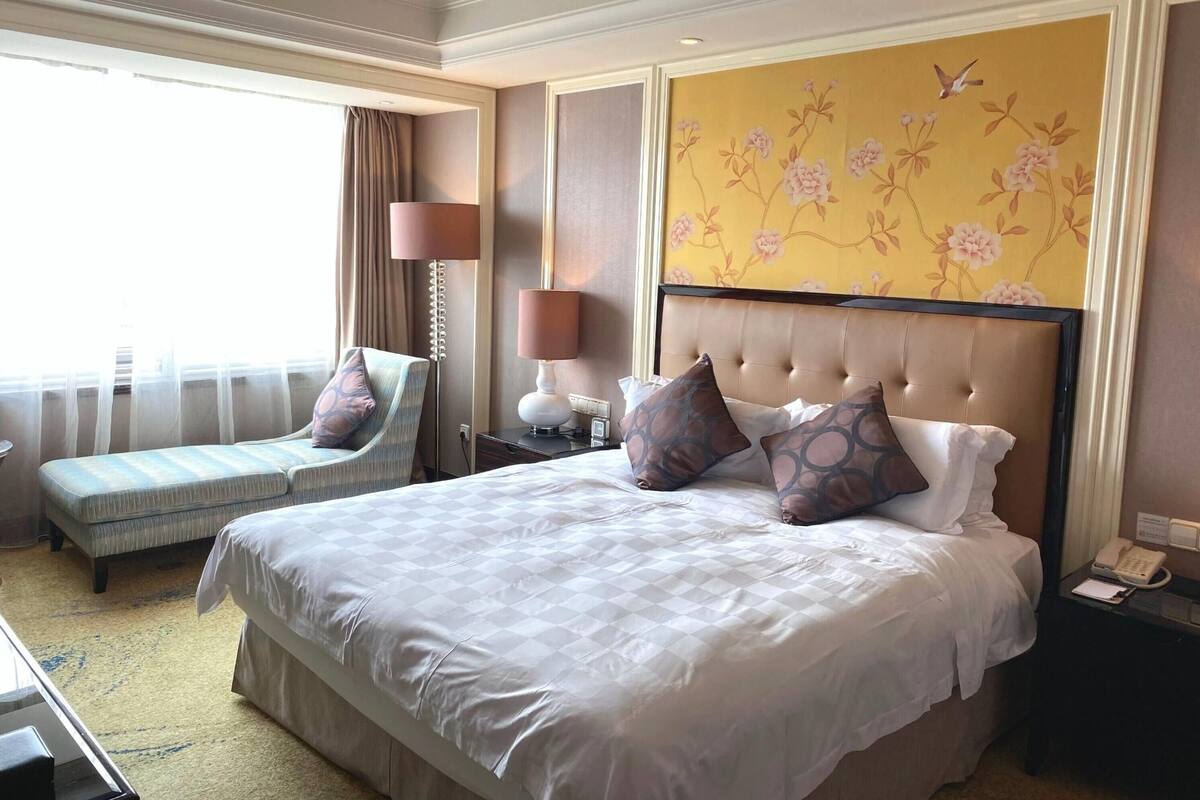 Una habitación de hotel con una cama grande, un sofá, una mesita de noche con lámpara y un adorno floral en la pared.