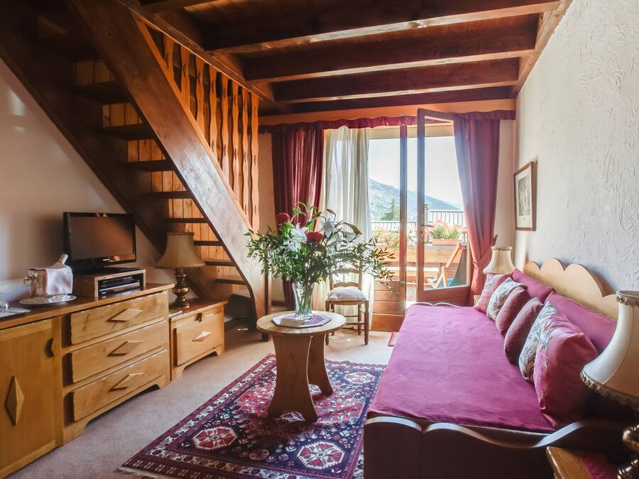 Une pièce chaleureuse avec un escalier en bois, un canapé recouvert d’un plaid rouge, une table ornée d’un vase et un téléviseur posé sur un meuble en bois.