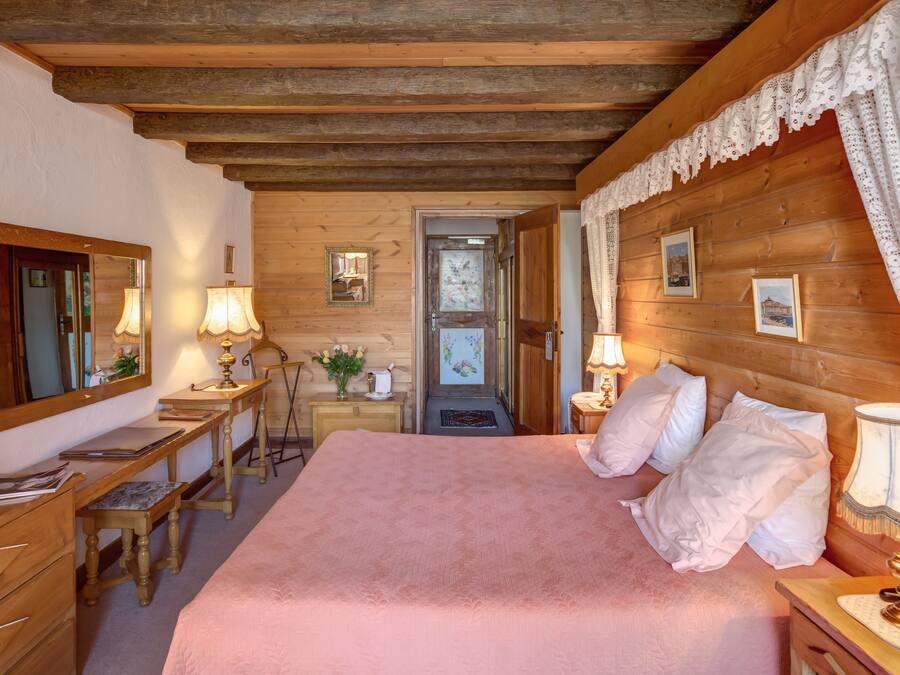 Un dormitorio acogedor con una cama grande, paredes de madera, un escritorio con lámpara y una puerta que da a otra habitación.