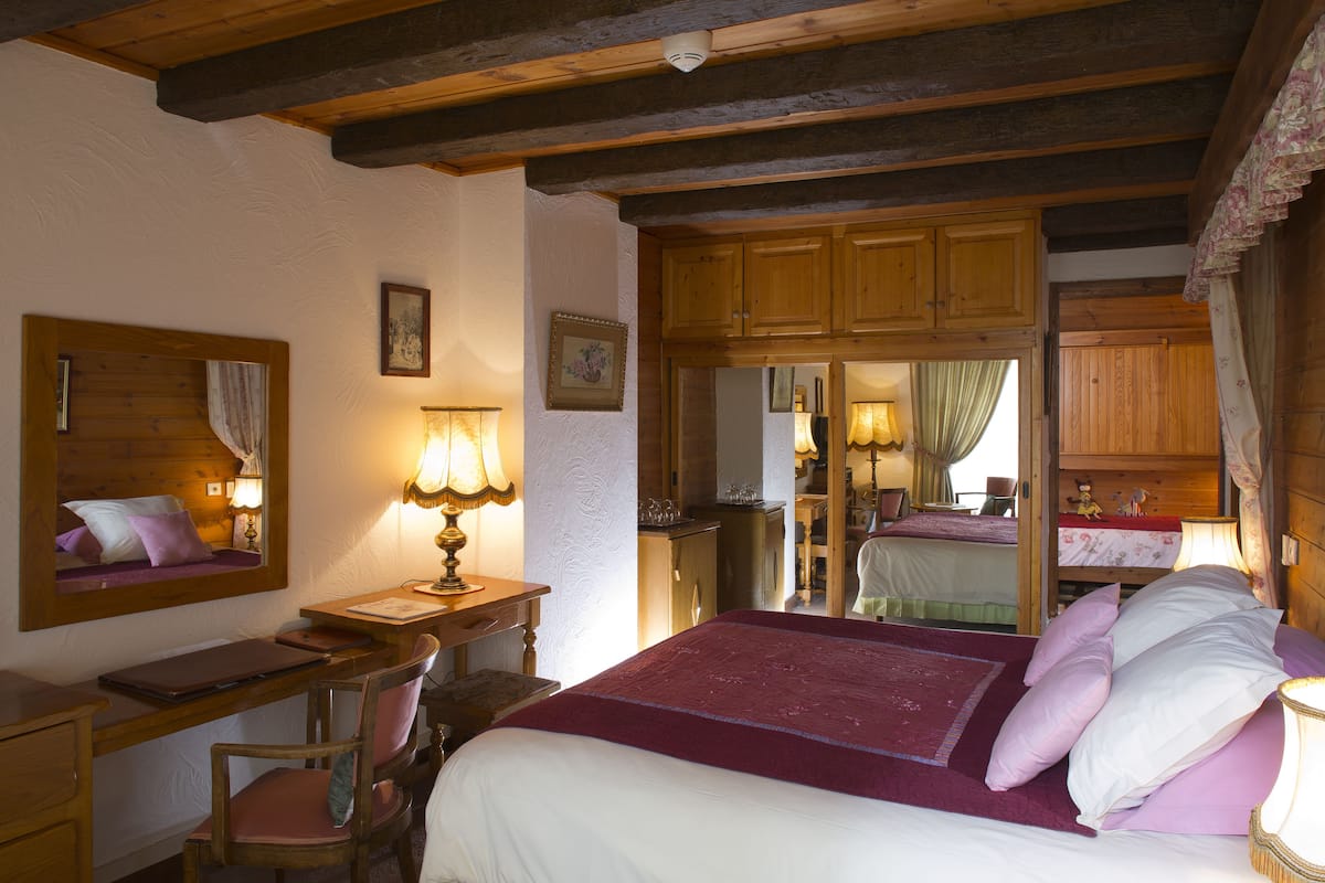 Une chambre à coucher avec un lit, un bureau et une chaise. Il y a un miroir au mur et une fenêtre avec des rideaux.