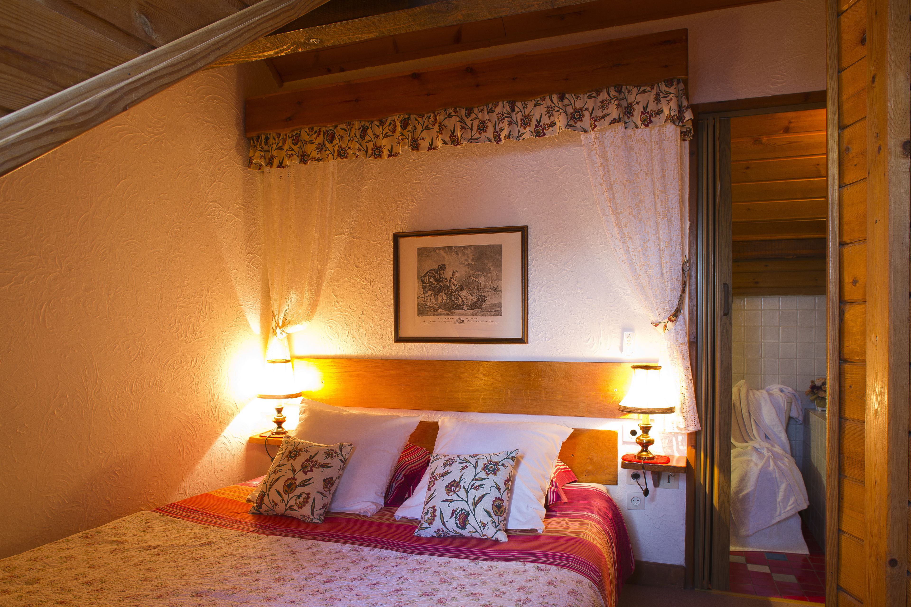 Ein Schlafzimmer mit einem Bett, zwei Nachttischlampen, einem gerahmten Bild an der Wand und einer Holztür.