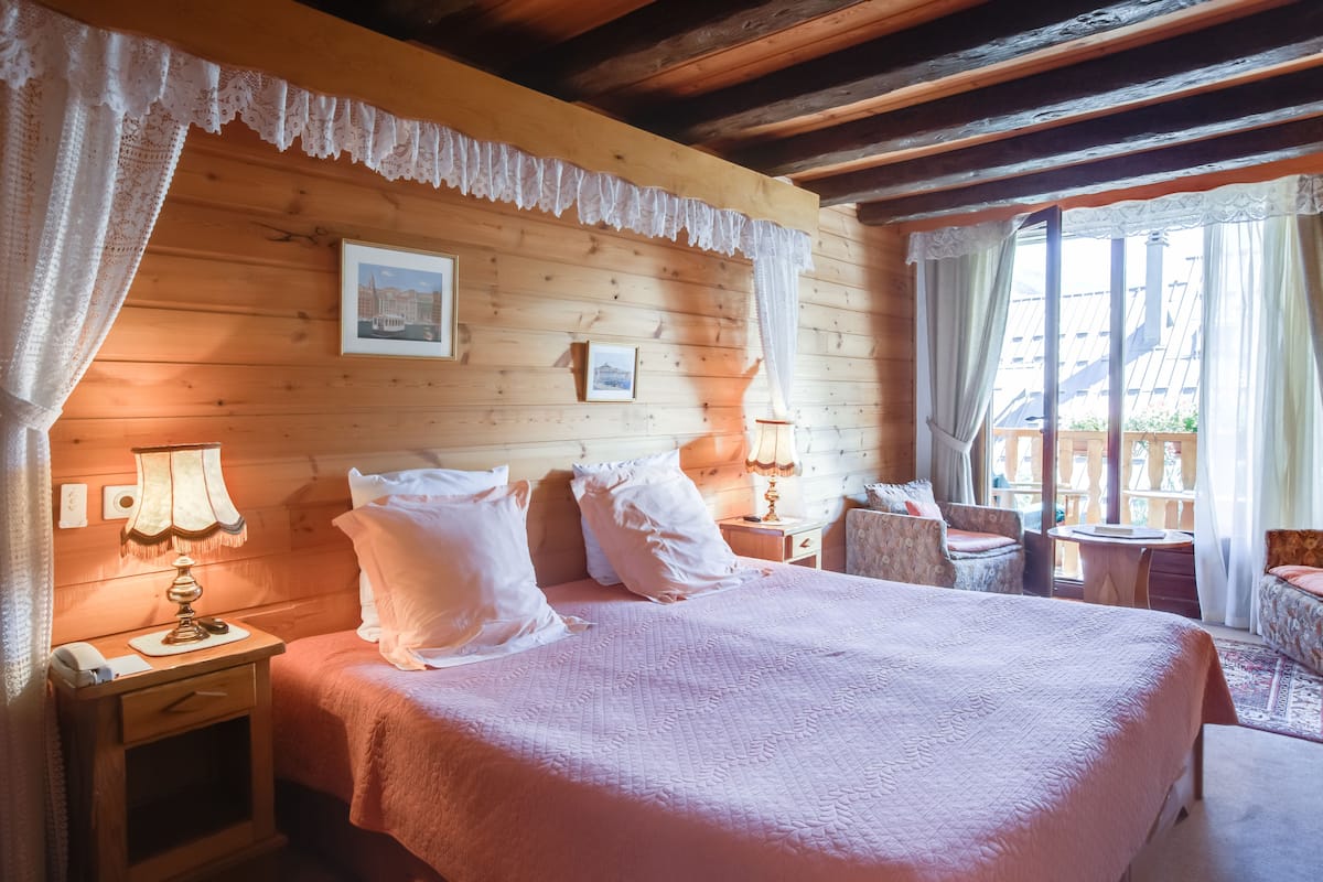 Une pièce chaleureuse, avec des murs en bois, comprenant un grand lit, deux tables de chevet avec des lampes, une chaise et une petite table.