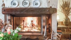 A cozy room with a fireplace, a wooden chair, and a table with a vase of flowers.