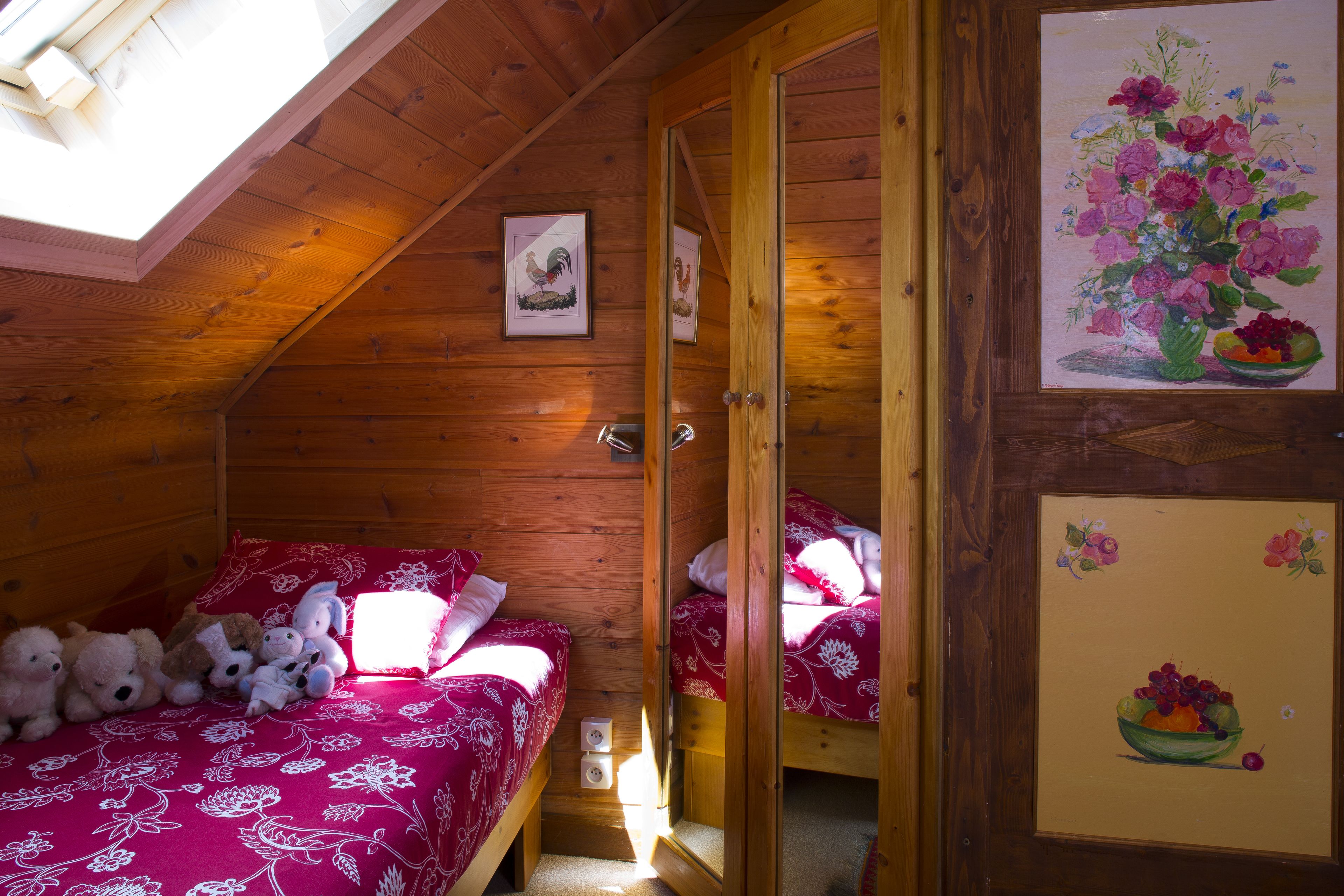 A cozy wooden cabin bedroom with two beds, a skylight, and artwork on the walls.