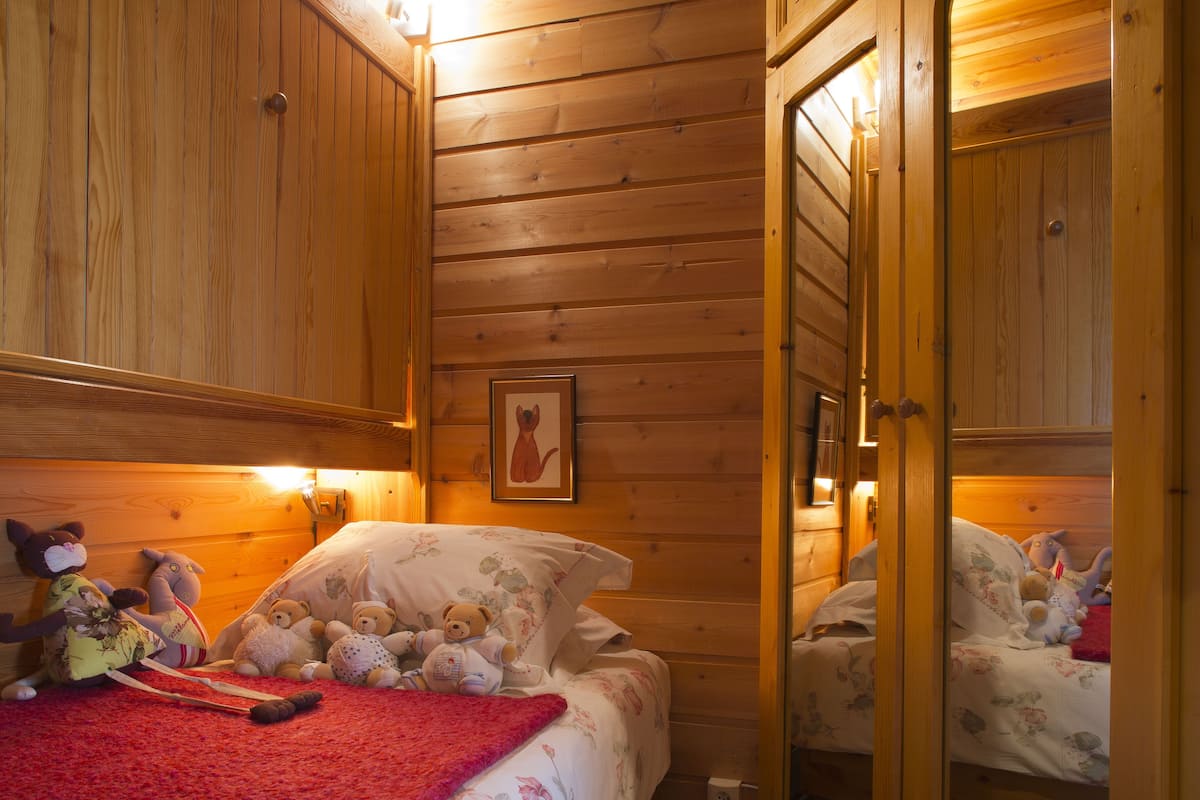 Une chambre dans une cabane en bois, avec un lit, des peluches et une couverture rouge.