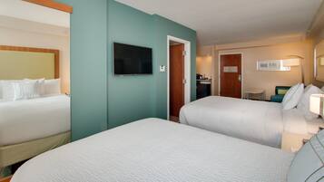 A hotel room with two beds, a TV, a desk with a chair, and a bathroom visible through an open door.