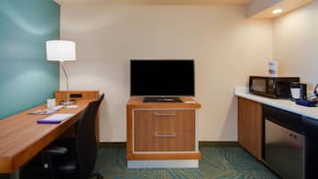 Habitación de hotel compacta con un escritorio de madera, un televisor de pantalla plana, microondas y un refrigerador pequeño.