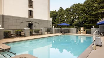 A swimming pool with a clear blue water, surrounded by a fence, and a building with a flat facade in the background.