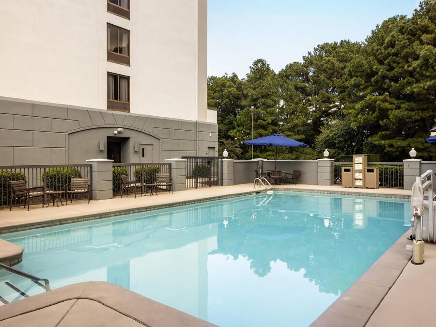 A swimming pool with a clear blue water, surrounded by a fence, and a building with a flat facade in the background.