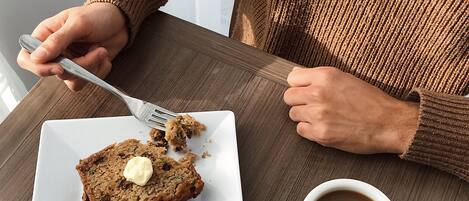 Une personne est assise à une table devant une assiette blanche remplie de nourriture et une tasse blanche.