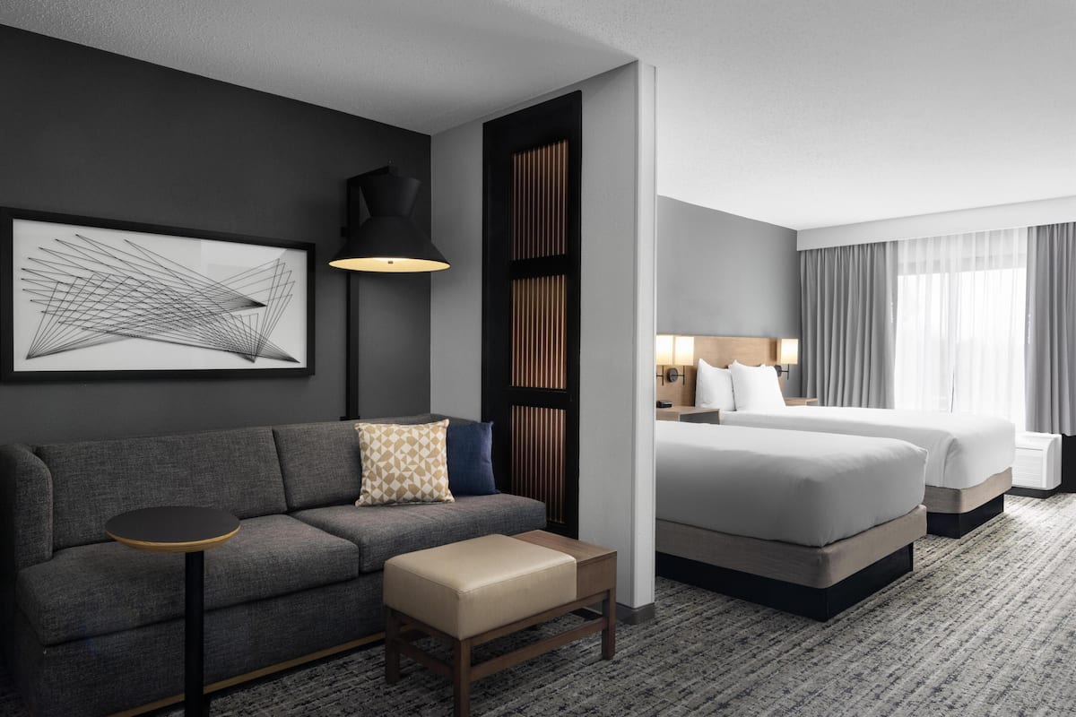 A hotel room with a sofa, a small table, a bed, and a large window with curtains.