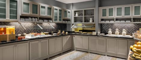 A modern kitchen with grey cabinets, a herringbone tile backsplash, and a buffet setup.