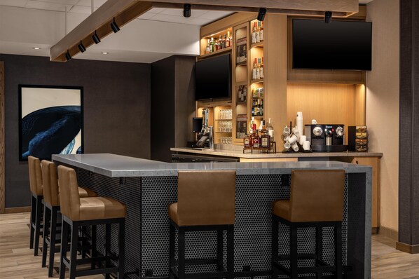 Un espace bar moderne avec un long comptoir, des tabourets de bar, un téléviseur et un meuble à boissons.