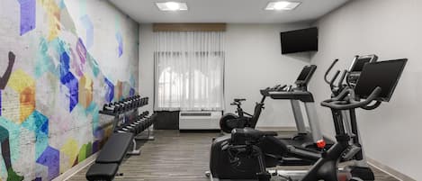 A gym with exercise equipment, a bench, a wall-mounted TV, and a window with curtains.