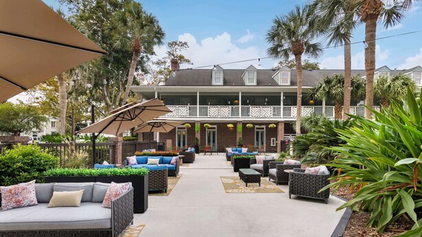 A courtyard with outdoor seating, a building with a balcony, and palm trees. - Best Western Plus St. Simons (St. Simons Island)