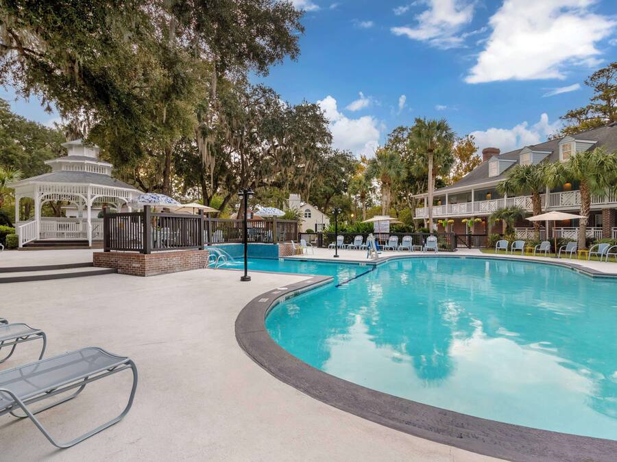 A pool area with lounge chairs, a gazebo, and a building with balconies.