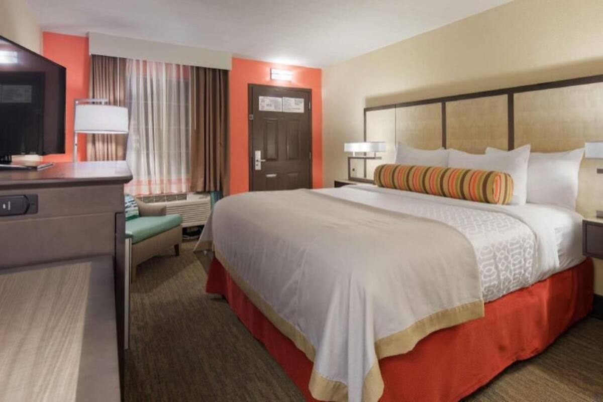 A hotel room with a bed, bedside tables, a desk with a computer, a TV, and a window with curtains.