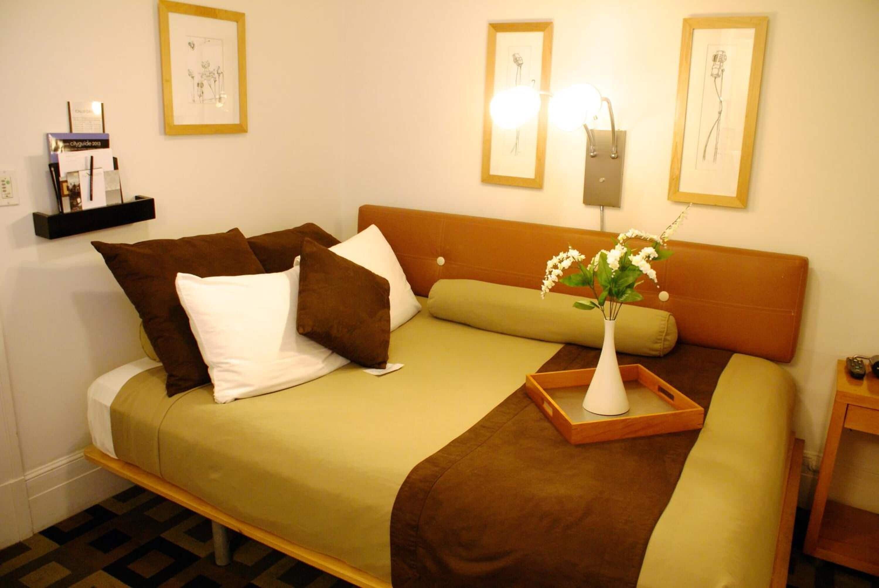 A neatly made bed with a brown headboard, a white vase with flowers, and a tray.