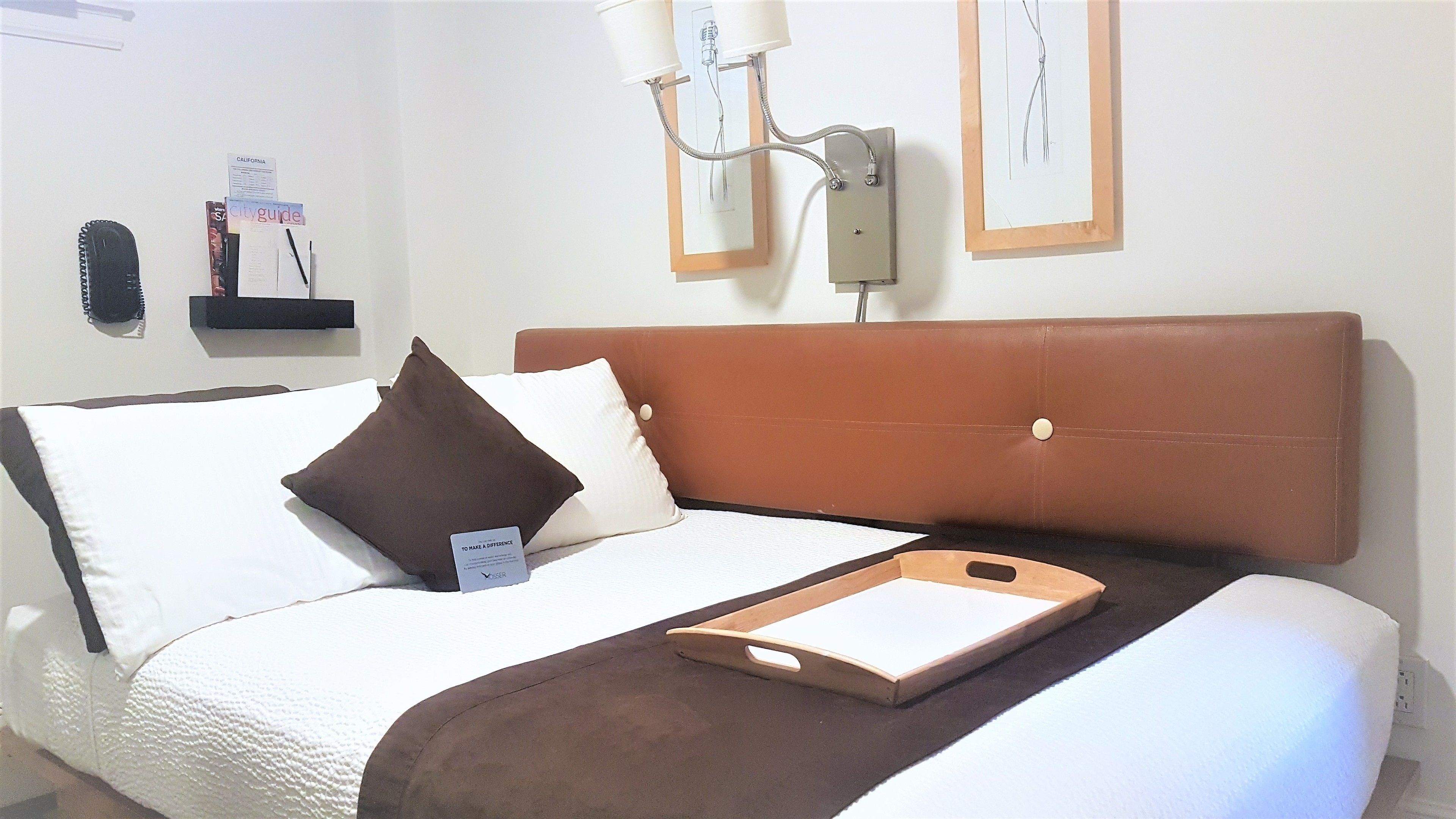 A neatly made bed with a brown headboard, a pillow, and a bedside table with a notepad and pen.