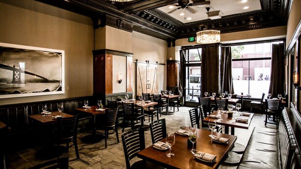 A restaurant with a classic interior, featuring wooden tables and chairs, chandeliers, and large windows with views outside.