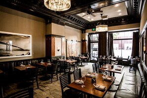 A restaurant with a classic interior, featuring wooden tables and chairs, chandeliers, and large windows with views outside. - The Mosser (San Francisco)