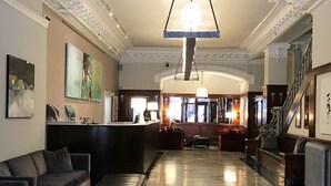 A spacious lobby with a marble floor, a reception desk, a staircase, and a large chandelier.