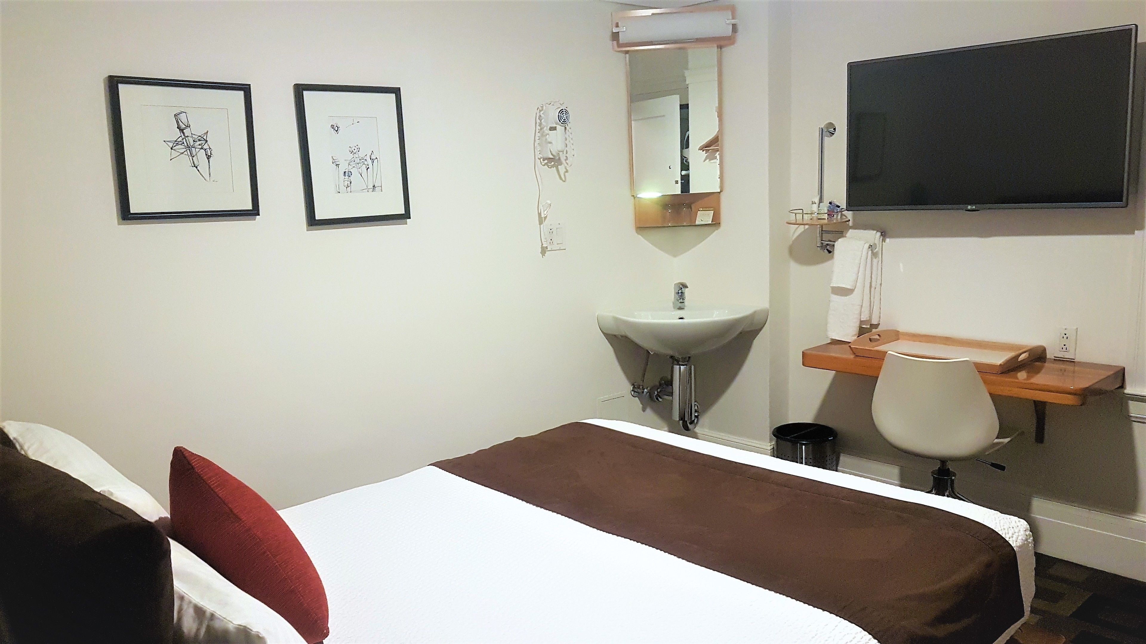 A hotel room with a bed, a desk, a chair, a sink, and a television.