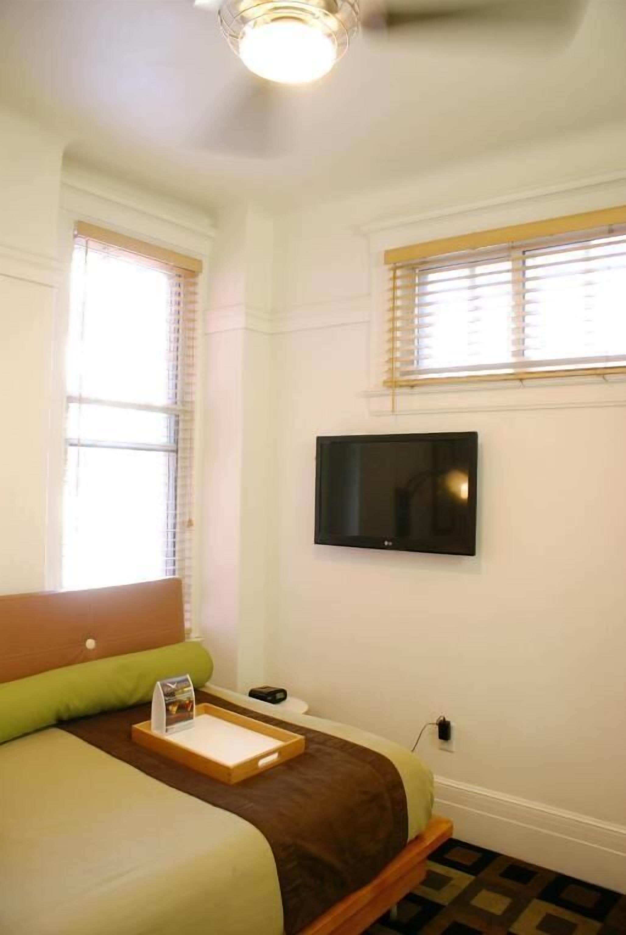 A hotel room with a bed, a TV mounted on the wall, and a window with blinds.