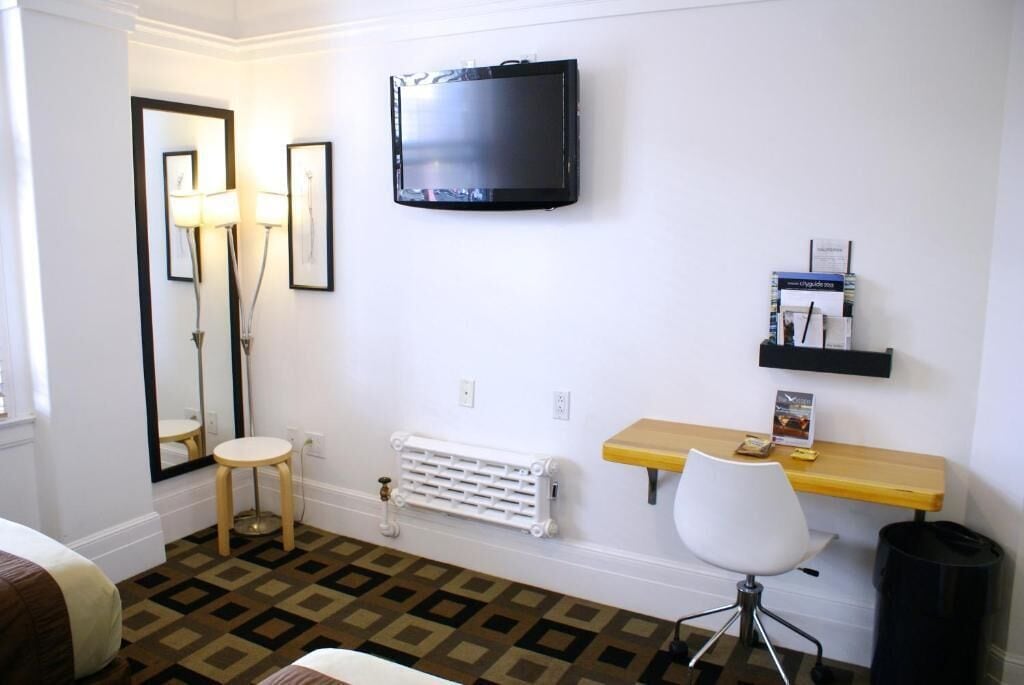 Une chambre d’hôtel comprenant un lit, un bureau avec une chaise, un radiateur, un téléviseur fixé au mur et une étagère avec des articles de toilette.