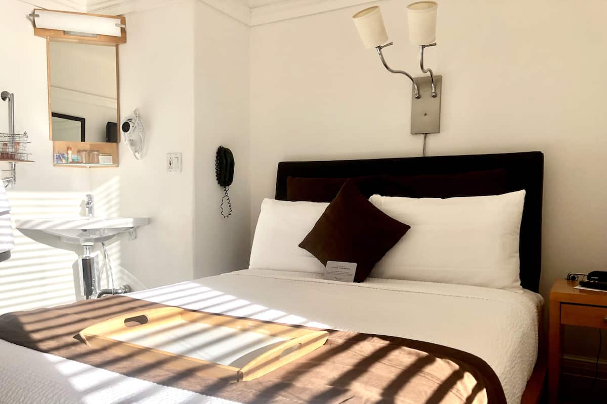 Una habitación de hotel con una cama, una mesita de noche, un teléfono instalado en la pared y un accesorio de luz en la pared.