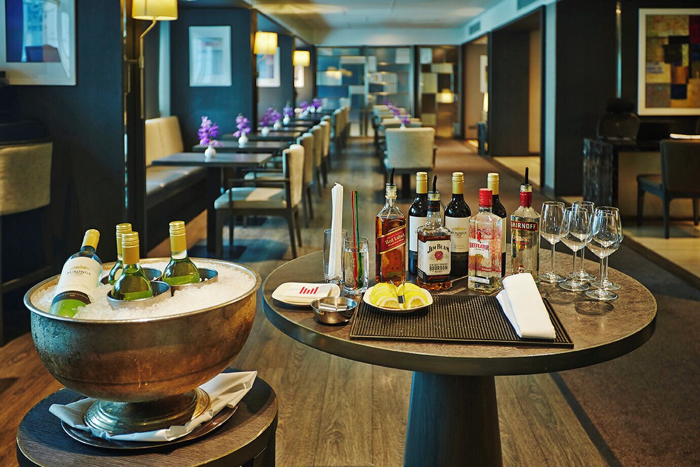 A hotel bar with a large copper bowl filled with bottles, a plate with lemon slices, and several glasses.