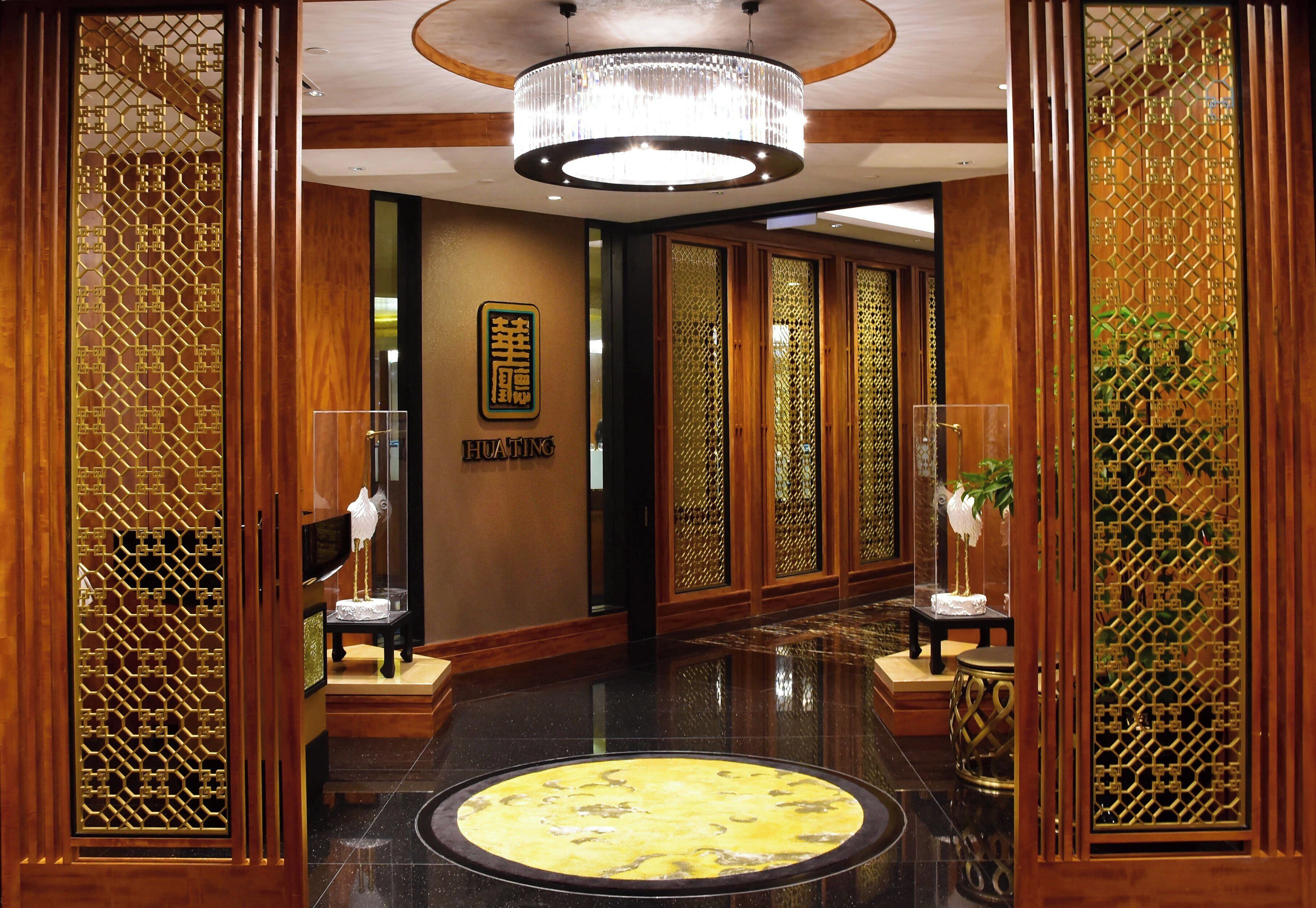 Een hotellobby met een ronde marmeren vloer, houten lambrisering en een kroonluchter.