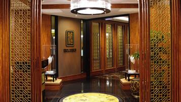 Een hotellobby met een ronde marmeren vloer, houten lambrisering en een kroonluchter.