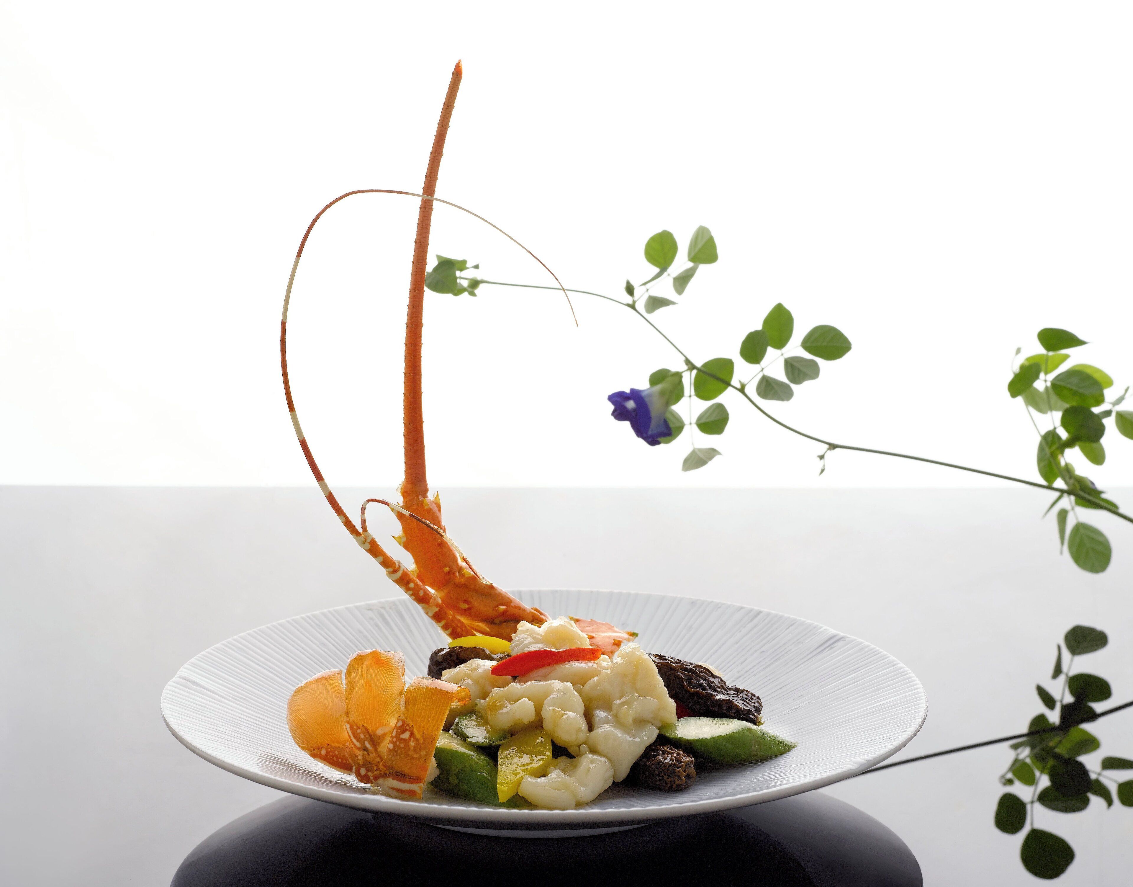 Ein Teller Essen mit einer dekorativen orangenen Zutat, Gemüse und einer violetten Blume.