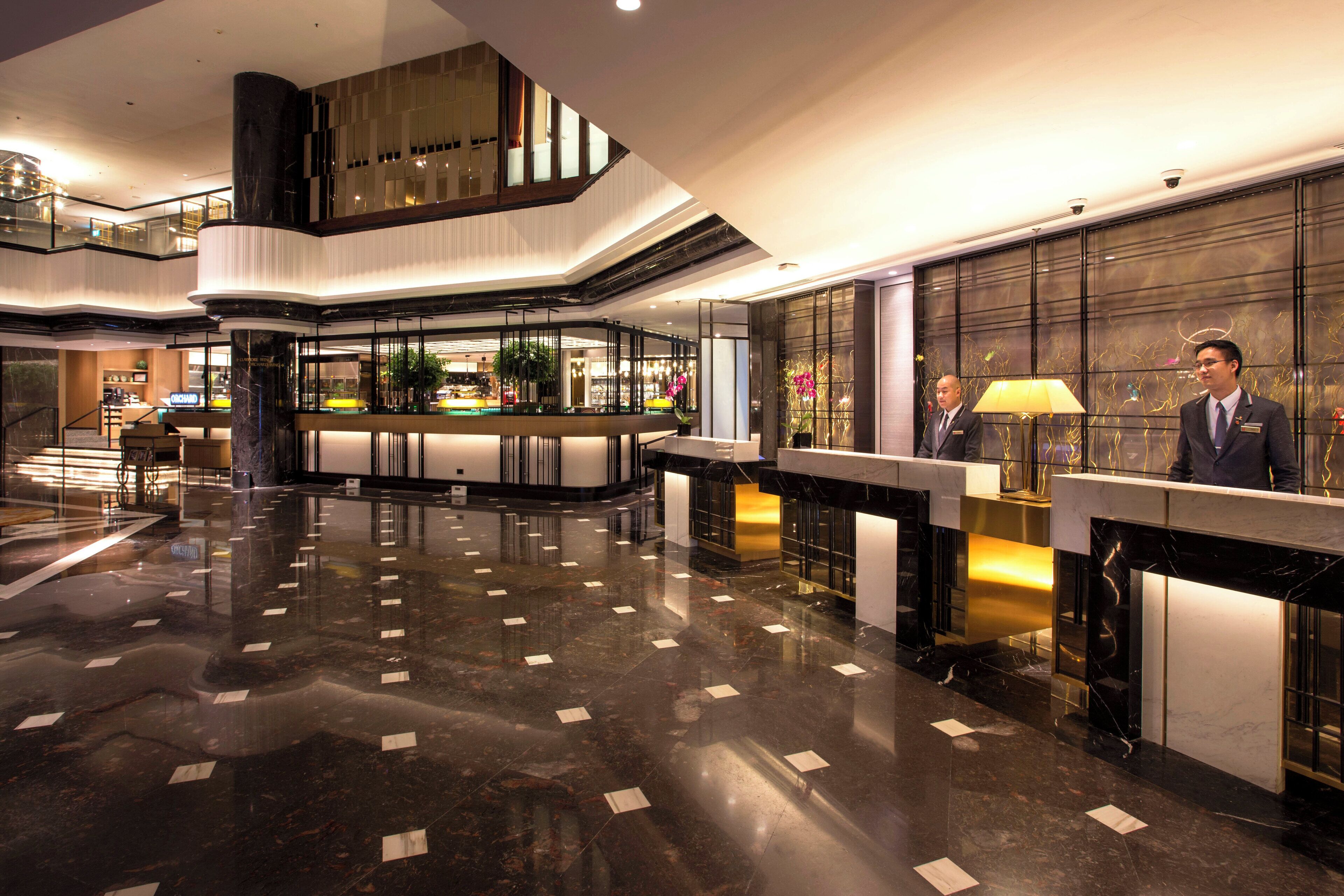 Eine moderne Lobby mit hochglänzendem Marmorboden, einem Empfangstresen und einer Treppe zu einer oberen Ebene.